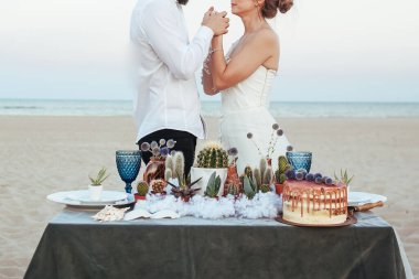Gelin ve damadın önünde kumsalda sulu süslemeli düğün masası. Düğün kaktüsü ve sulu süslemeler. Sahilde tören. Deniz kenarında parti.