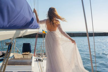 Gelin elbiseyi yatın güvertesinde tutuyor. Rüzgâr gelinliği ve gelinin saçını sallıyor. Genç bir kadının bakış açısı. Tekneyle düğün gezisi.