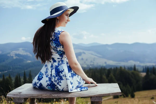 Jovem mulher em vestido elegante descansando no banco nas montanhas — Fotografia de Stock