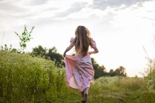 Menina correndo através do campo em um vestido rosa — Fotografia de Stock