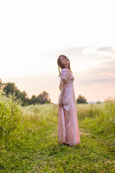 Девушка, стоящая в поле в розовом платье — стоковое фото