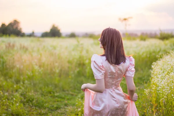 Menina de pé no campo em um vestido rosa — Fotografia de Stock