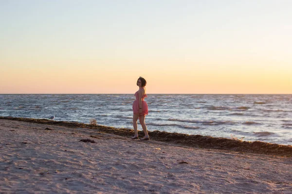 Una chica vestida de rosa camina por una playa vacía al amanecer. — Foto de Stock