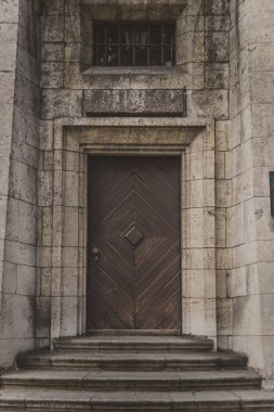 Büyük taş duvarda, merdivenleri ve küçük penceresi olan eski kahverengi ahşap kapı.