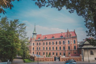 Turuncu tuğla duvarlı ve kırmızı çatılı Neo-Gotik bina.