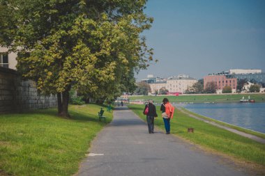 İnsanlar güneşli bir günde Krakow 'daki Wisla Nehri' nin gezinti güvertesinde yürür.