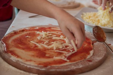 El, tahta kesme tahtasına serpiştirilmiş peynirli pizza koyar.