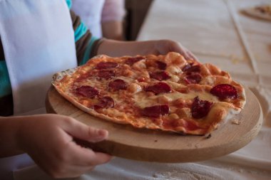 Kadınların elleri, tahta kesme tahtasına un serpiştirilmiş pizzayı tutuyor.