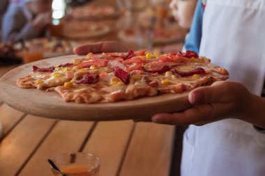 Kadınların elleri, tahta kesme tahtasına un serpiştirilmiş pizzayı tutuyor.