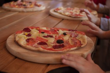 Kadınların elleri, tahta kesme tahtasına un serpiştirilmiş pizzayı tutuyor.