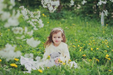 Bahar kiraz bahçesinde bir kız oyuncak ayı tutuyor.