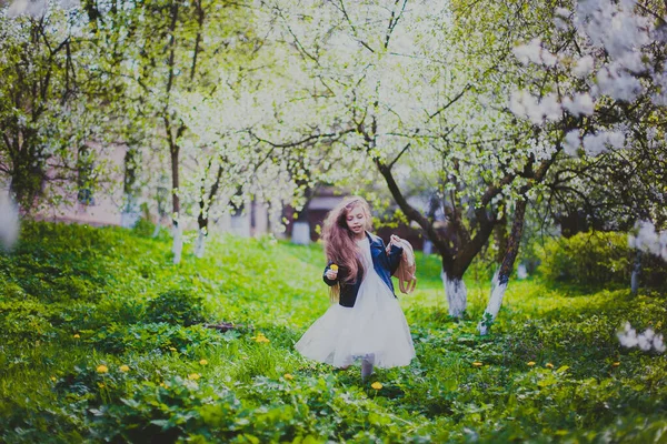 Menina em jaqueta preta e vestido branco correndo no jardim de cereja primavera — Fotografia de Stock