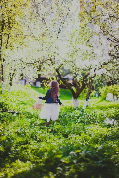 Dziewczynka w czarnej kurtce i białej sukience biegająca w wiosennym wiśniowym ogrodzie — Zdjęcie stockowe