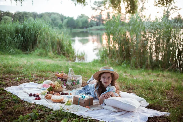 Dziewczyna w słomkowym kapeluszu jest na pikniku w parku nad brzegiem rzeki. — Zdjęcie stockowe