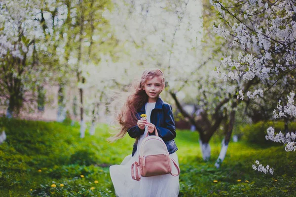 Niña en chaqueta negra y vestido blanco corriendo en el jardín de cerezos de primavera — Foto de Stock