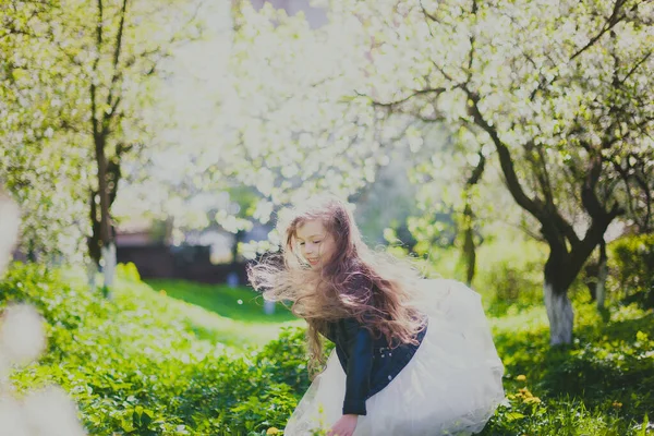 Маленькая девочка в черной куртке и белом платье танцует в весеннем вишневом саду — стоковое фото