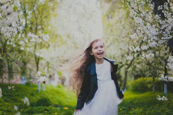 Menina em jaqueta preta e vestido branco correndo no jardim de cereja primavera — Fotografia de Stock