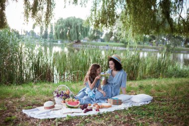 Nehrin kıyısındaki parkta piknik yapan bir anne ve kız.