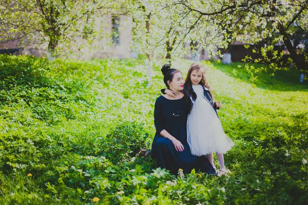 En liten flicka kramar sin mor i vårens körsbärsträdgård — Stockfoto