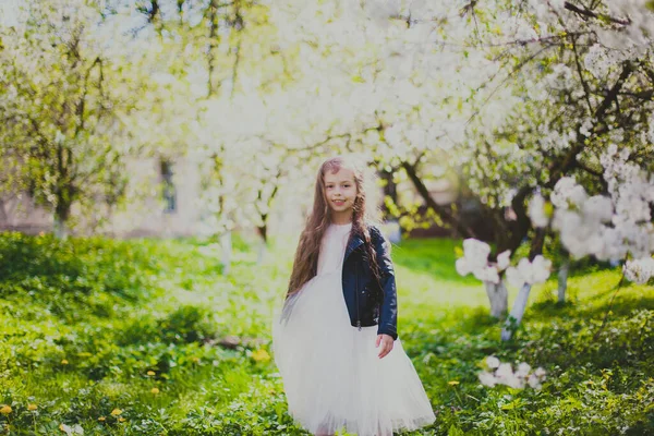 Menina em jaqueta preta de pé e sorrindo no jardim de cereja primavera — Fotografia de Stock