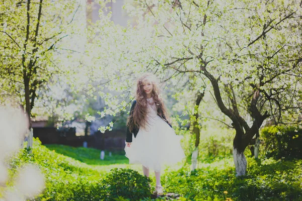 Niña en chaqueta negra y vestido blanco de pie en el jardín de cereza de primavera —  Fotos de Stock