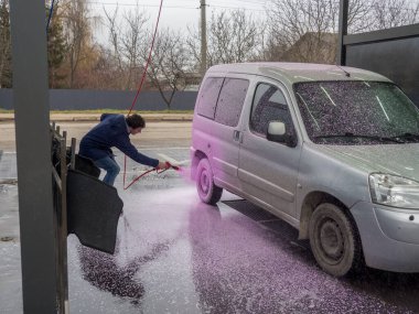 Bir adam oto yıkamada pembe köpükle araba kaplıyor.
