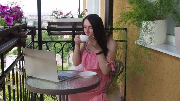 집에서 원격으로 일하는 발코니에 커피를 마시며 노트북 컴퓨터를 사용하고 있습니다 — 비디오