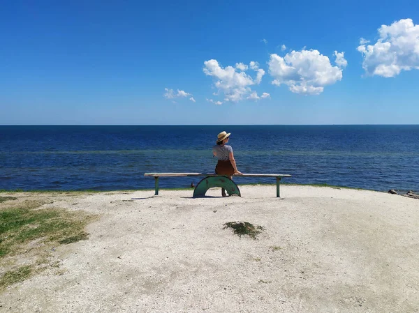 Vrouw met strohoed zittend aan zee op de bank op zonnige zomerdag — Stockfoto