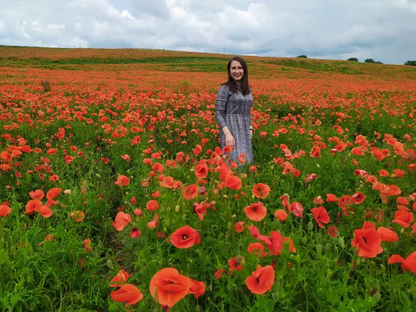 Mulher sorridente em um vestido cinza longo em pé no campo de papoula vermelha — Fotografia de Stock