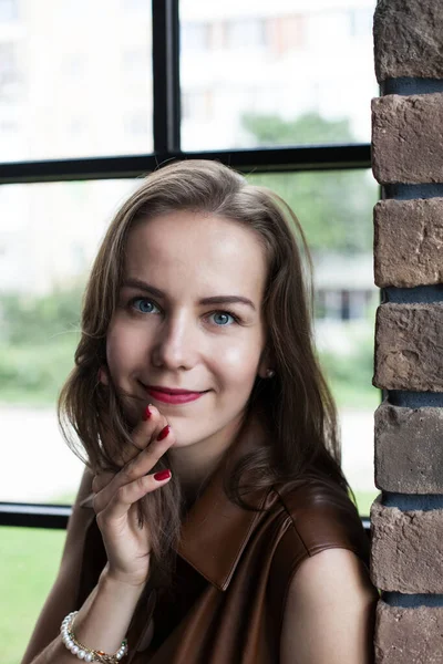 Schöne junge Frau im braunen Lederkleid sitzt auf der Fensterbank — Stockfoto