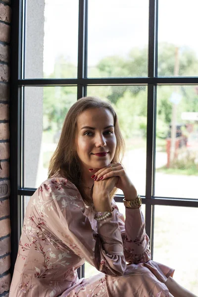 Schöne junge Frau in rosa Kleid sitzt auf der Fensterbank — Stockfoto