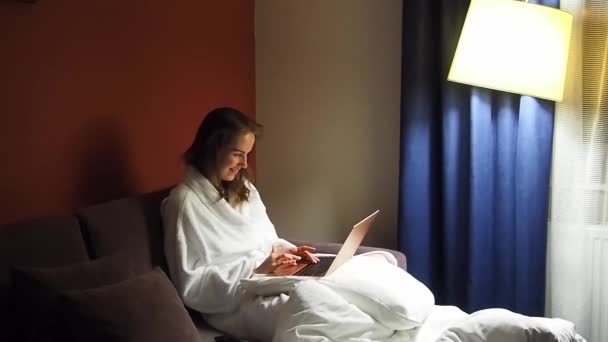 Zakelijke vrouw met een laptop in een hotelkamer gekleed in een badjas — Stockvideo