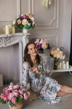 Çiçeklerin arasında bir odada oturan güzel genç bir kadın.