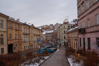Lublin, Polonya, 25 Kasım 2025: Eski bir kasabada kar zemini kaplıyor. Renkli binaların yanındaki yolda park halindeki arabalar..