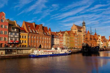 Gdansk, Polonya, 27 Kasım 2025: Gdansk 'ta nehir kıyısındaki parlak binalar. Tekneler mavi bir gökyüzünün altında suda yüzerler. Gündüz oldu ve bölge hareketli..