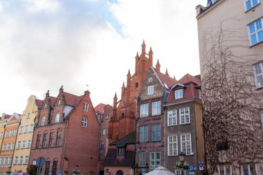 Eski binalar, Gdansk şehrinin çatıları arasında yükselen yüksek bir kuleyle cadde boyunca uzanır. Gökyüzü parçalı bulutlu.