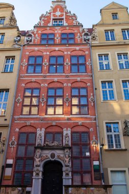 Gdansk 'ta detaylı oymaları ve büyük pencereleri olan kırmızı tuğlalı bir bina. Sahne, güneşli bir günde şehir yaşamını gösteriyor..