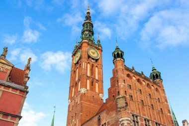 Polonya 'nın Gdansk kentindeki bir meydanda belediye binasının saat kulesi duruyor. Açık mavi gökyüzünün altında binalar var.. 