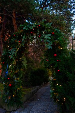 Bir patika, kış akşamı yeşil yapraklar, süsler ve ışıklarla kaplı bir kemer yoluna sahiptir. Gdansk, Polonya