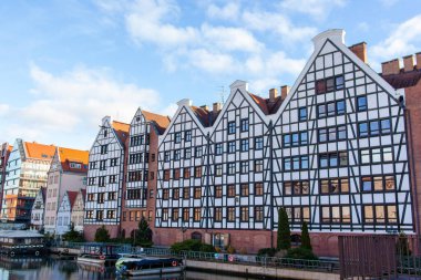 Güneşli bir günde Gdansk 'ta bir kanalın yanında farklı mimarisi olan eski binaların yanından geçeceğiz. Tekneler yakındaki suda yüzer..