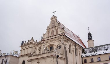 Polonya, St. Joseph Kilisesi, Lublin. Çatısı karla kaplı küçük bir kasabada tarihi bir kilise duruyor. Sahne bulutlu gökyüzü ile kışın geçer. Kilisenin detayları.