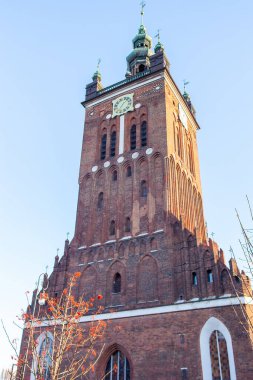 St Catherine Kilisesi Polonya 'nın Gdansk kentindeki en eski kilisedir. Uzun bir tuğla kilise kulesi açık mavi gökyüzüne karşı yükseliyor. Güneş ışığı binanın üzerine düşerken saat zamanı gösterir..