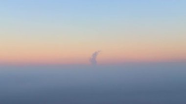 Kalın bir sis tabakasının üzerinde yükselen bir bulut oluşumu görülüyor. Güneş batarken gökyüzü renk değiştirir, alacakaranlıkta güzel bir doğa manzarası yaratır..