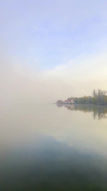 Sabahın erken saatlerinde sis gölün üzerinde yuvarlanır. Evler kıyıya yakın, kısmen gözden uzak. Su sisi ve çevresindeki doğayı yansıtır. Ivano-Frankivsk, Ukrayna