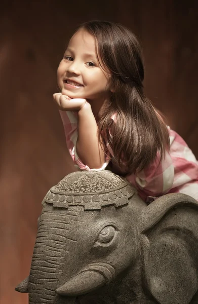 Girl with dark hair sitting on a stone elephant — Zdjęcie stockowe