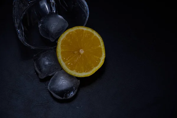 Siyah zemin üzerinde limon ve buz küpleri olan bir cam.