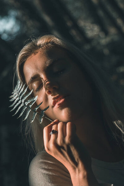 Autumn girl with a leaf of tender fern in her hands covering her face from the sun's rays