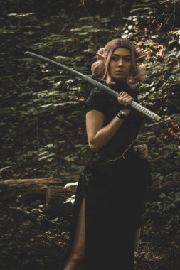 Elinde katana olan bir elf kızı ormanda yürüyor ve savaşa hazırlanıyor.