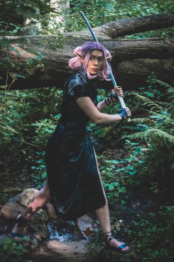 Elinde katana olan bir elf kızı ormanda yürüyor ve savaşa hazırlanıyor.