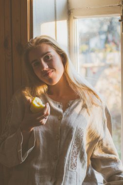 Tatlı kız elma yiyor ve pencerenin kenarında güneşleniyor.